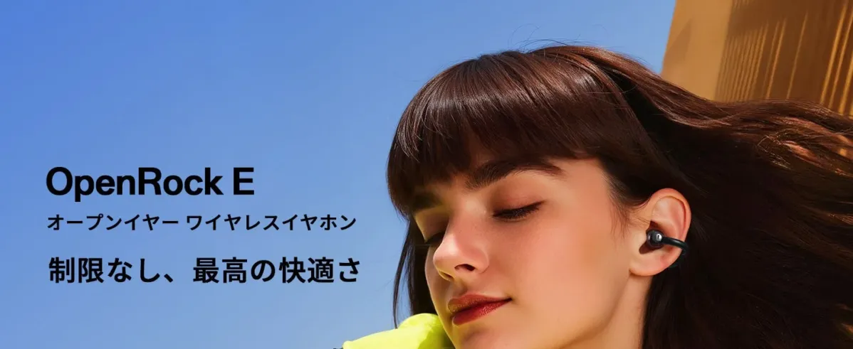 青空の下、OpenRock Eのオープンイヤーワイヤレスイヤホンを装着した女性のポートレートです。
