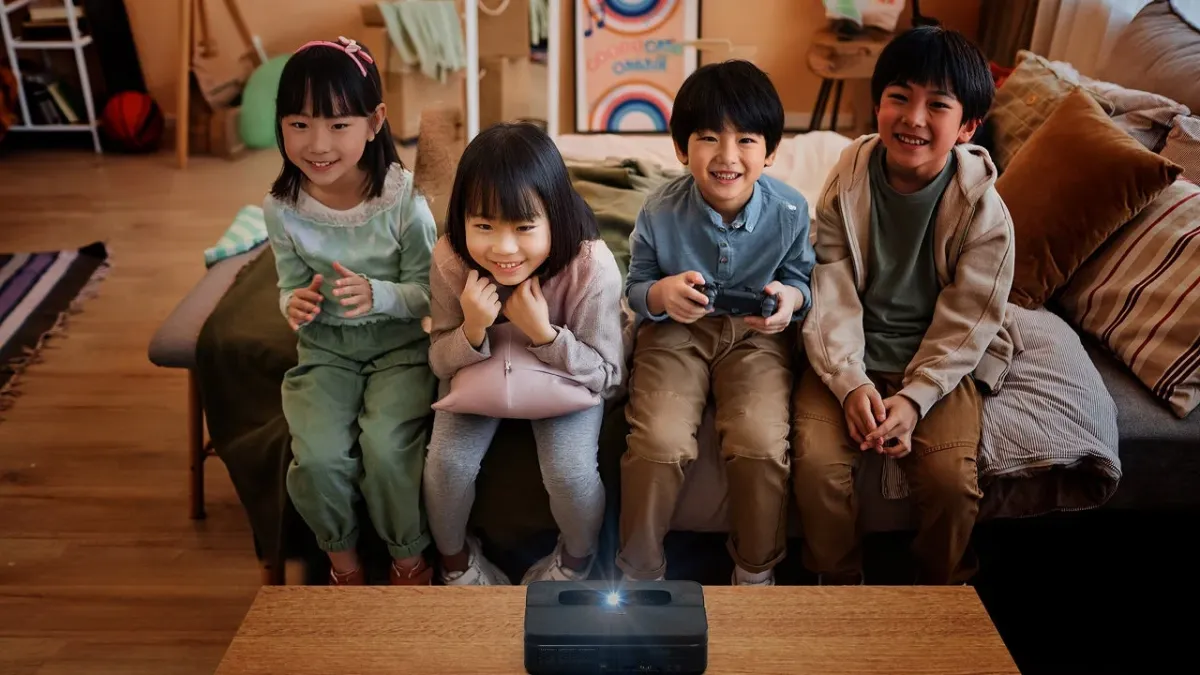 リビングルームで4人の子供たちが楽しそうに集まっています。コーヒーテーブルに置かれたプロジェクターを使ってゲームをプレイしており、皆笑顔でリラックスした雰囲気です。