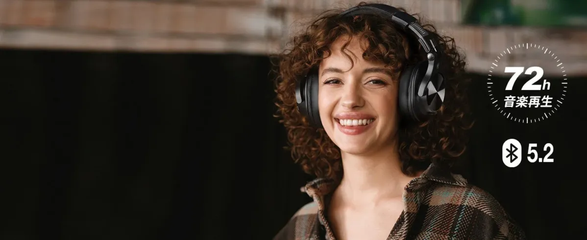 黒いヘッドホンを装着し、笑顔でカメラを見つめる巻き毛の女性。