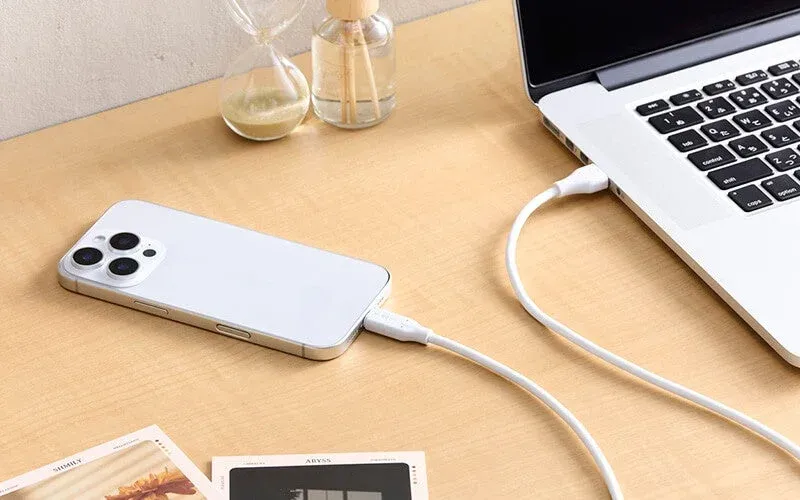 木製のデスク上で、白いスマートフォンがUSBケーブルでノートパソコンに接続されています