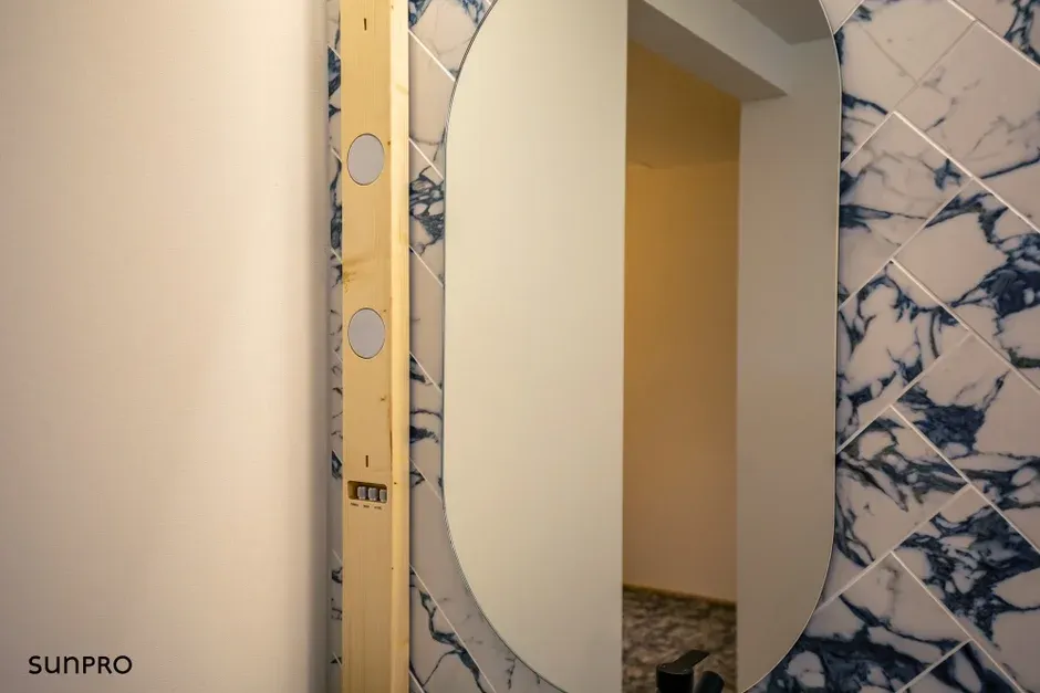 青と白の大理石調タイルが特徴的な壁に設置された楕円形の鏡