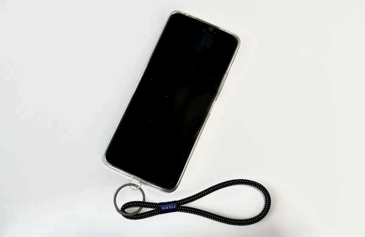 白い背景に置かれた、透明なケースを装着したスマートフォンと、それに接続された黒いリストストラップ