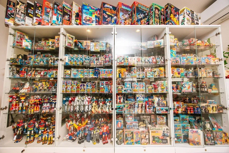 ガラスケースに陳列された、日本のヴィンテージロボット玩具の壮大なコレクション。超合金シリーズや懐かしいアニメのヒーローロボットが箱入りで多数並び、ロボット玩具文化の歴史が感じられる。