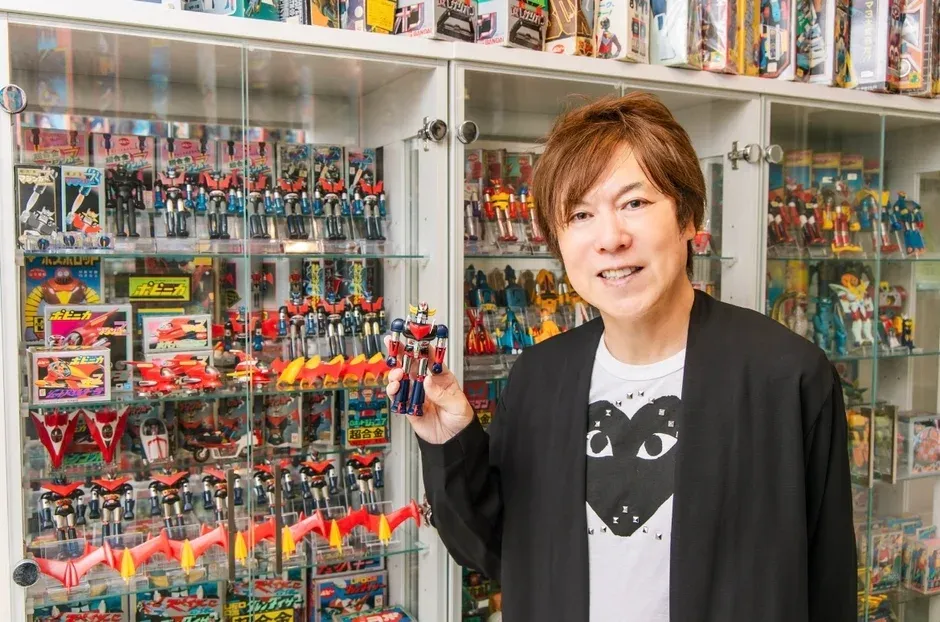 多くのヴィンテージロボット玩具が並ぶガラスケースの前で、一人の男性がロボットフィギュアを手に笑顔を見せています。マジンガーZやグレートマジンガーなどの超合金シリーズが多数展示されており、コレクターの情熱が伝わる一枚です。