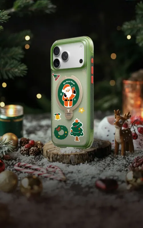 雪が積もった台座に、サンタクロースやクリスマスモチーフのステッカーが貼られた緑色のスマートフォンケースが置かれている画像