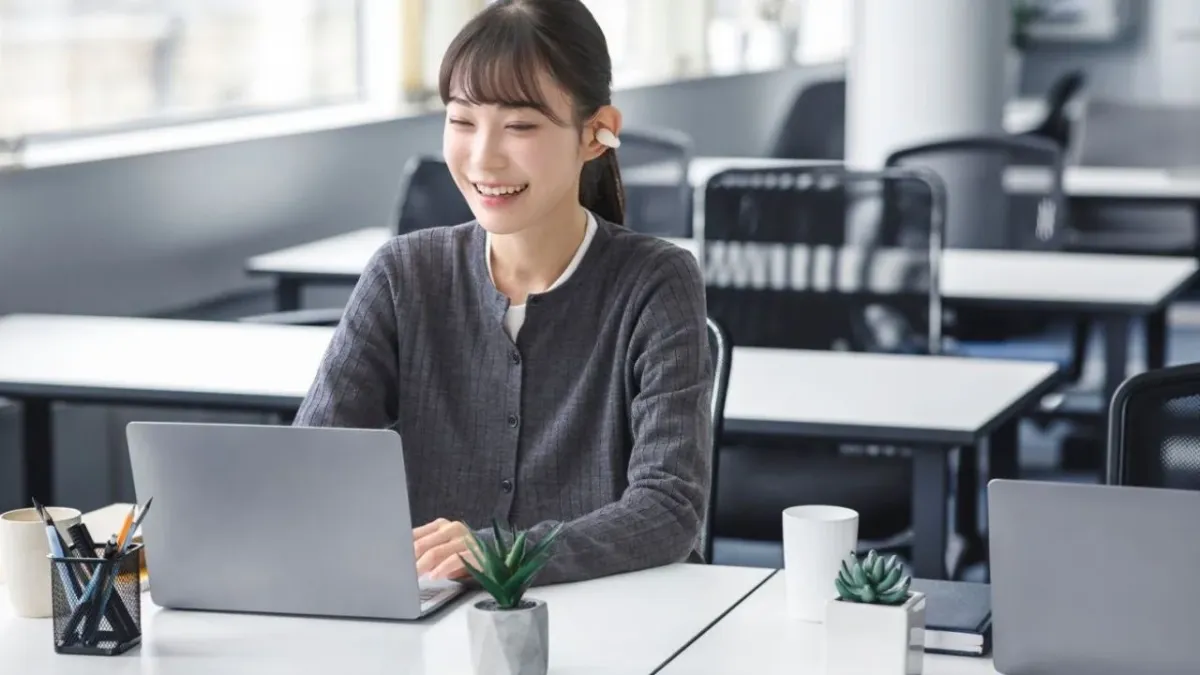 オフィスでノートパソコンを操作しながらイヤホンを装着している女性