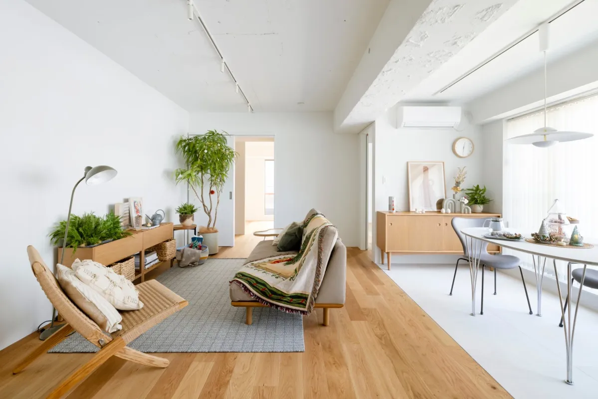 白を基調とした明るく広々としたリビングダイニングルームです。木の床と白い壁が特徴で、北欧モダンな家具や観葉植物が配置され、居心地の良い空間を演出しています。