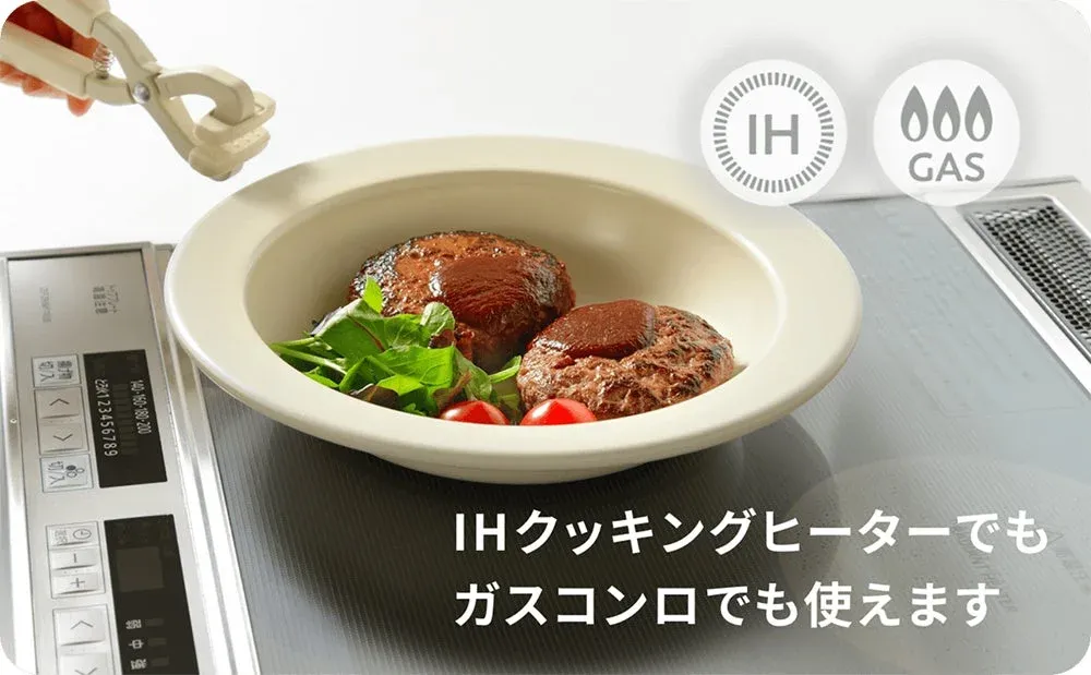 IHクッキングヒーターの上に置かれた皿に、ハンバーグとサラダが盛り付けられている。IHとガスコンロ両方で使えることを示すアイコンとテキストがあり、調理器具の汎用性を表現。手元にはトングが見える。