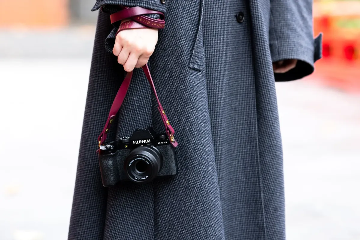 FUJIFILM X-S10とワインレッドのレザーストラップを持った人物