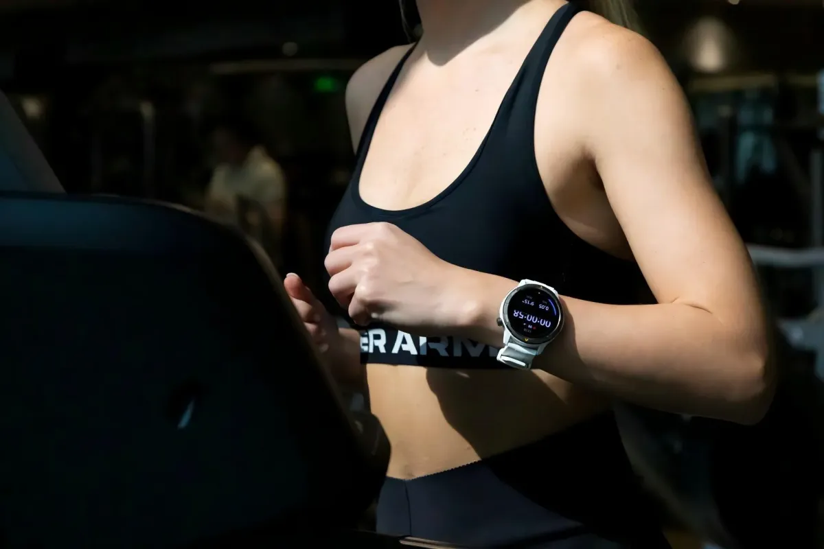 ジムでトレッドミルを使って運動している女性の姿です。彼女はスポーツブラを着用し、腕には運動データを表示するスマートウォッチをつけています。