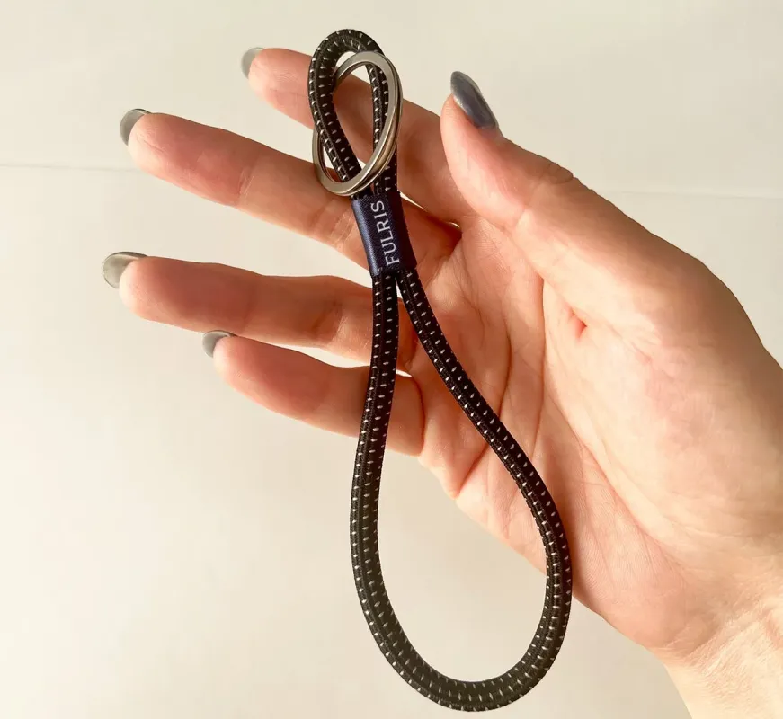 女性の指が、銀色のリングと「FULRIS」のロゴが付いた黒い斑点模様のループ状のストラップを掴んでいる様子