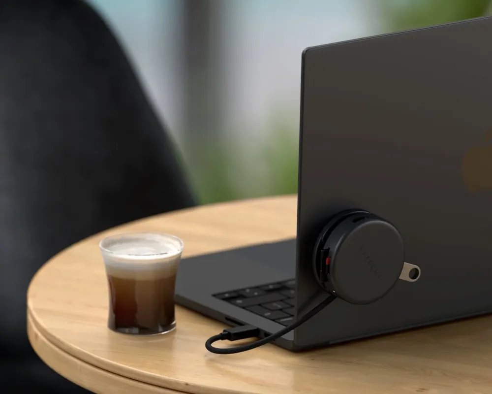 木製のテーブルに置かれた黒いラップトップの側面にSatechi製の丸いUSBハブが接続