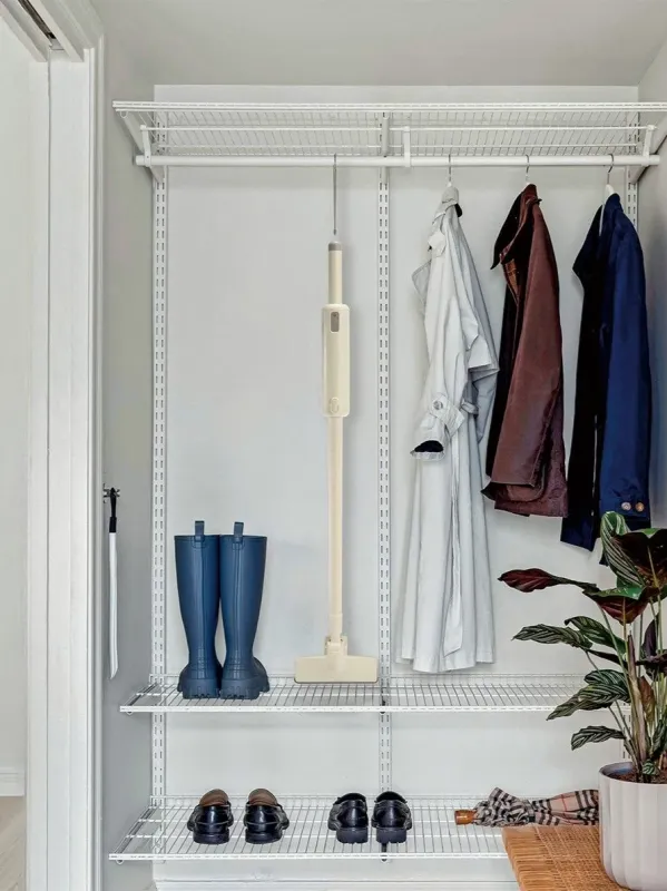 白いワイヤーラックで整理されたクローゼットまたは玄関収納の様子です。コートやジャケットがハンガーにかかり、下段には長靴や革靴、コードレス掃除機、観葉植物などがきれいに並べられています。