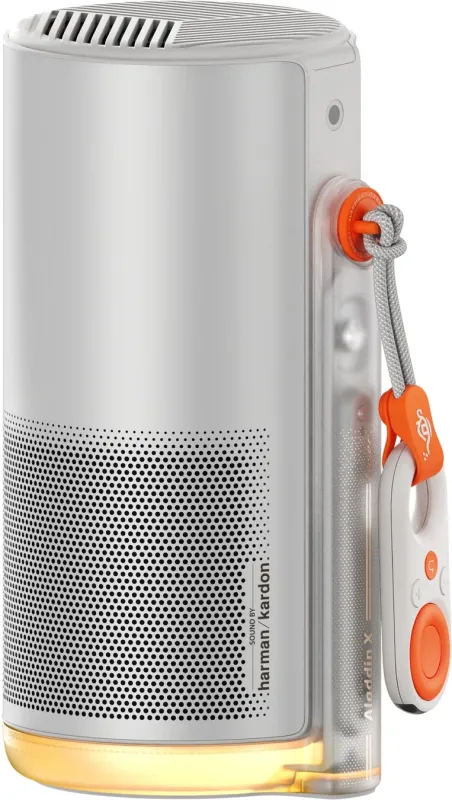 白を基調とした円筒形のスマートプロジェクター兼スピーカー。底部には照明があり、「SOUND BY harman/kardon」と「Aladdin X」のブランド名が見られます。オレンジ色のリモコンが付属し、多機能なモダンデザインの家庭用デバイスです。