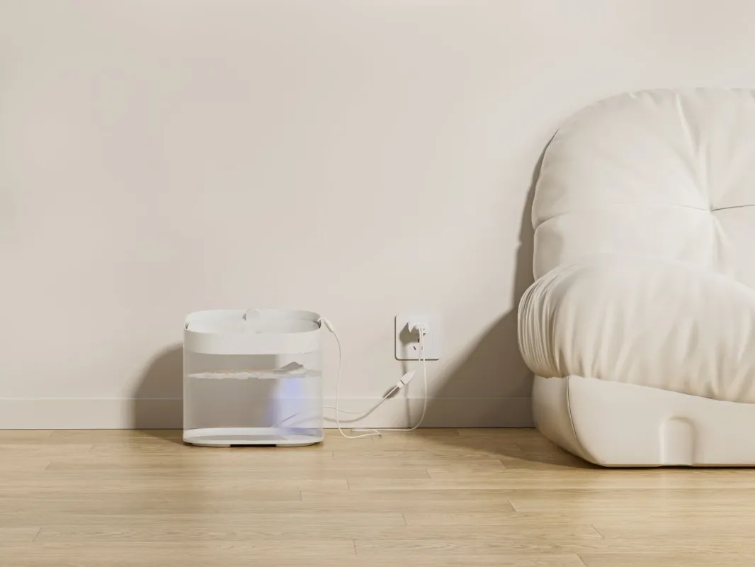 木製のフローリングに置かれた白いペット用自動給水器が、壁のコンセントに接続されている様子。右側には白いソファの一部が見え、シンプルでモダンなリビング空間が表現されています。