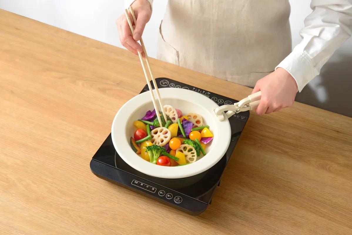IHクッキングヒーターの上に置かれた鍋で、色とりどりの野菜を調理している様子です。箸を使って野菜を混ぜており、健康的で手軽な料理のシーンが伝わります。