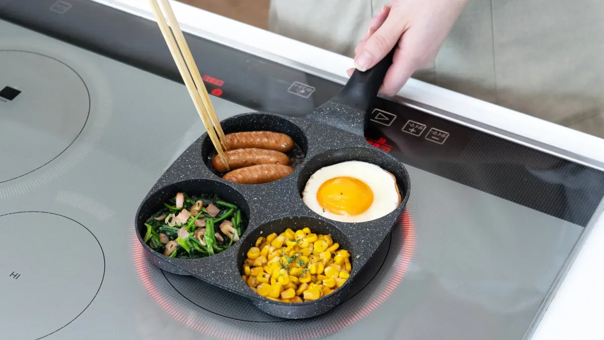 IHクッキングヒーターの上で、仕切り付きフライパンを使ってソーセージ、目玉焼き、ほうれん草炒め、コーンを同時に調理している様子。