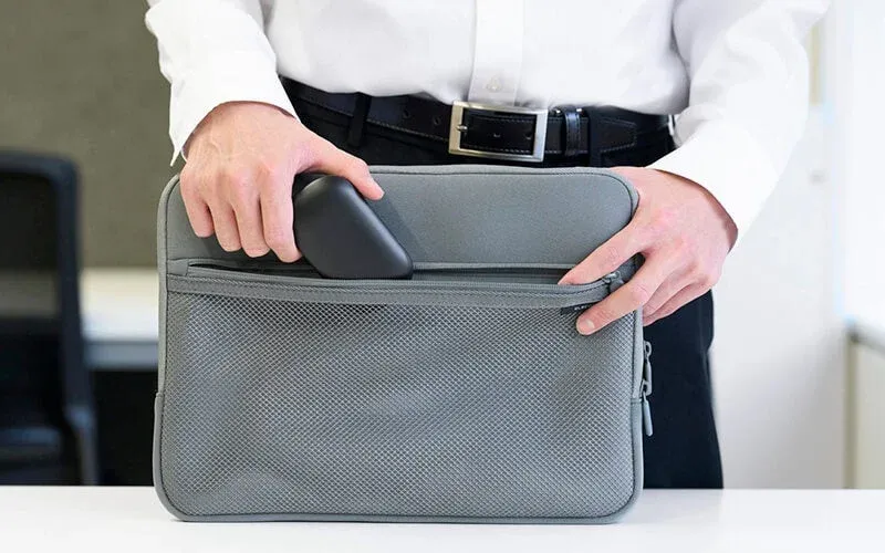 白いシャツを着た人物が、グレーのノートPC用スリーブのメッシュポケットに黒いガジェットを収納しています