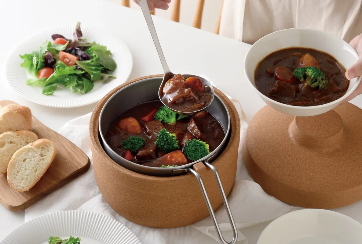 温かいビーフシチューが食卓に並べられ、お玉で器に盛り付けられている様子。付け合わせのサラダやパンも添えられ、美味しそうな食事が準備されている家庭的な風景です。