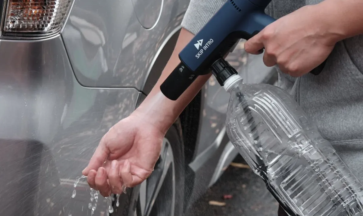 人がペットボトルに取り付けられたポータブルスプレーで車に水をかけている様子