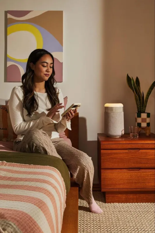 ベッドでスマートフォンを操作する女性の傍らに置かれたスマートスピーカー