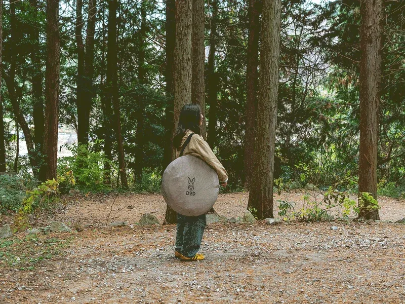 テントを背負い森に立つ人物