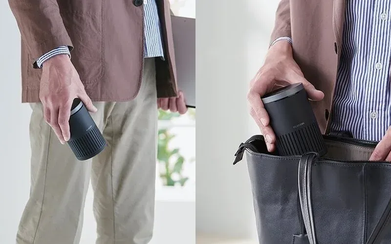 男性が黒い円筒形のポータブルデバイスを手に持ち、その後、黒いビジネスバッグに収納している様子を捉えた画像です。製品の携帯性とデザイン性を強調しています。