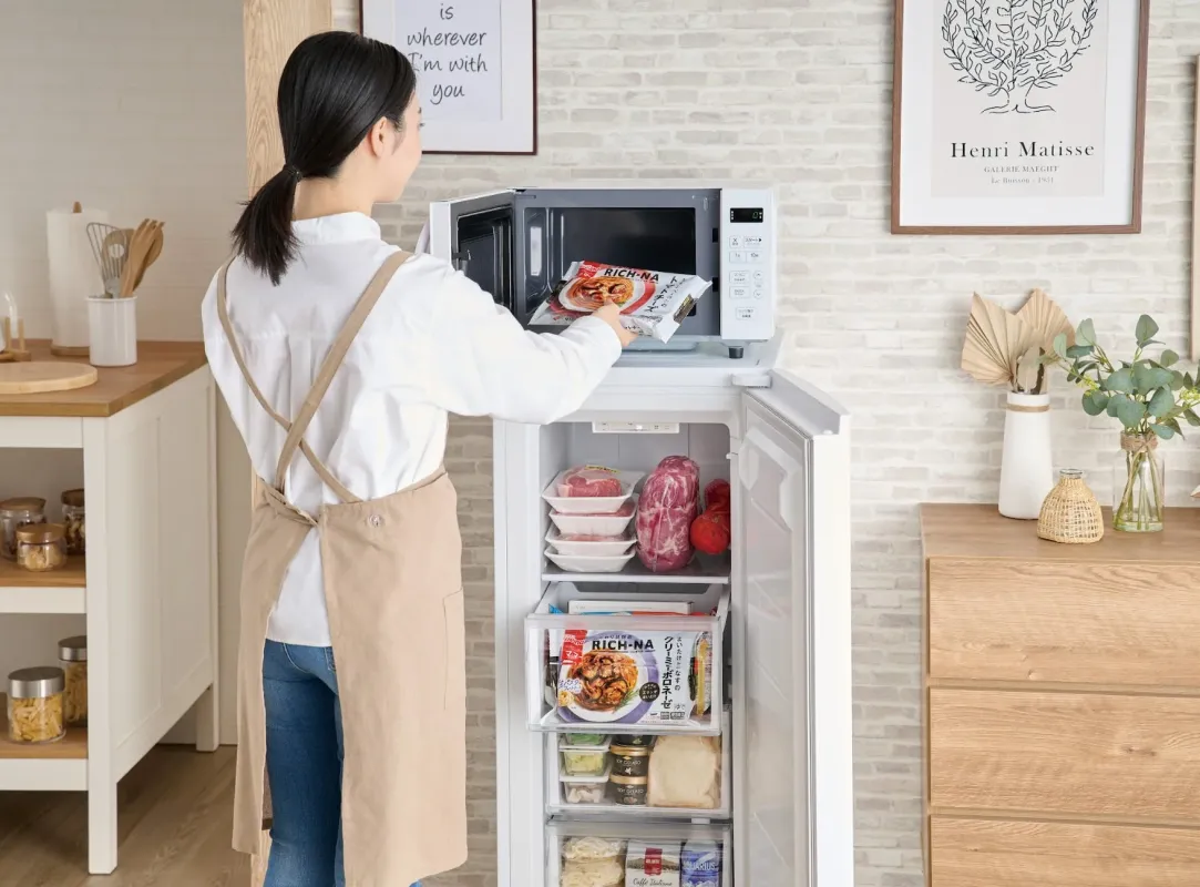 女性が冷凍庫の上に置かれた電子レンジに冷凍食品を入れているシーン