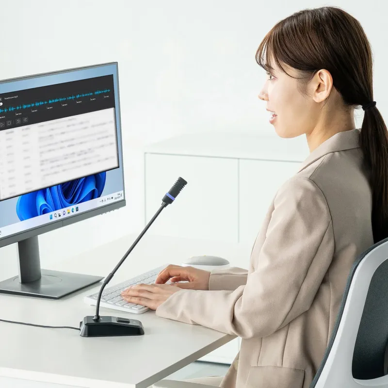 オフィスで女性がグースネックマイクに向かって話し、パソコンで作業している