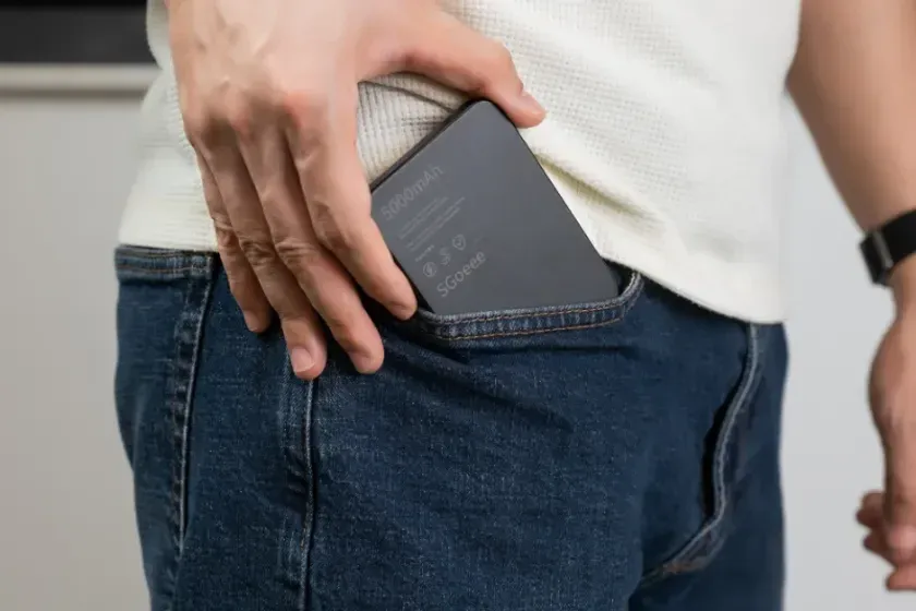 男性が黒いモバイルバッテリーをジーンズのポケットに入れている様子