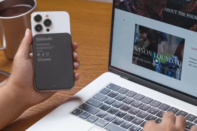 スマートフォンに装着されたモバイルバッテリーを手に持ち、ノートパソコンの画面を見ている様子