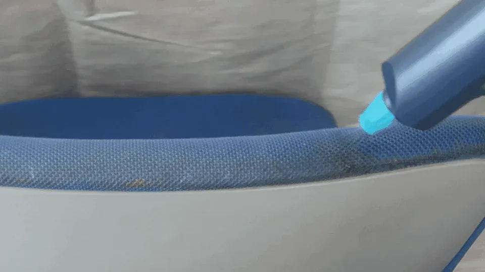 青い布張りの椅子の縁に付着した汚れを、青いクリーニングツールで掃除している様子を捉えた画像です。細かいゴミが確認できます。