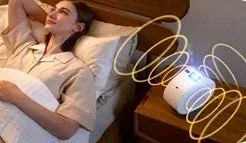 ベッドでリラックスしている女性の傍らに、何らかの信号を発している白いデバイスが置かれている様子。