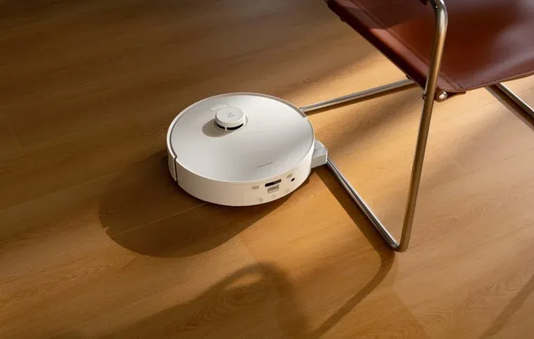 白いロボット掃除機が木製の床で椅子の近くを掃除する様子
