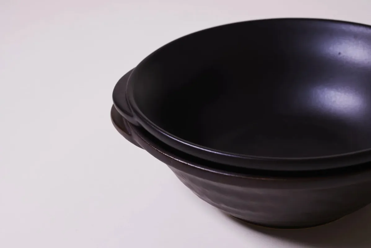 白い背景に、重ねて置かれた2つの黒い土鍋が写っています。シンプルで落ち着いた雰囲気の食器です。