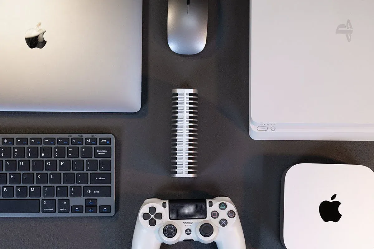 MacBook、Mac Mini、PlayStationなどが並べられたデスク上のフラットレイ