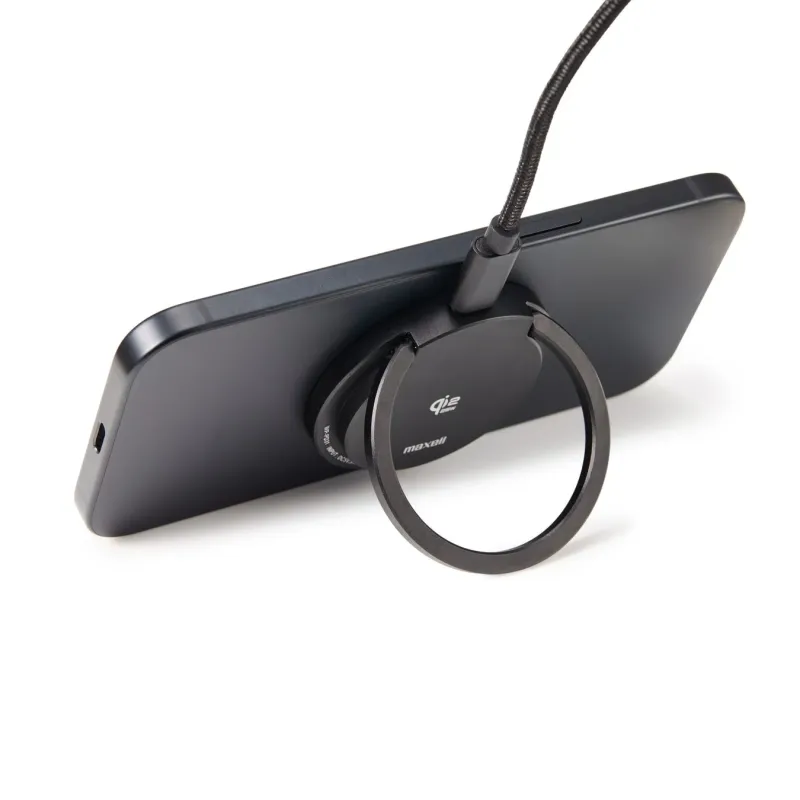黒いスマートフォンが横向きに置かれ、背面に装着されたリングスタンドで支えられています。USB-Cケーブルが接続されており、ワイヤレス充電機能も備えているようです。