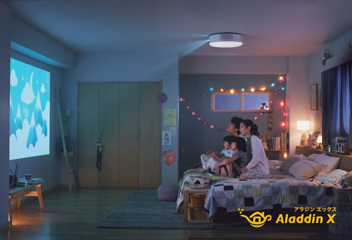 天井照明プロジェクター「Aladdin X」で壁に映し出された映像を、家族4人がベッドでくつろぎながら鑑賞している。カラフルな飾り付けがされた寝室で、温かい団らんのひとときを過ごしている様子。