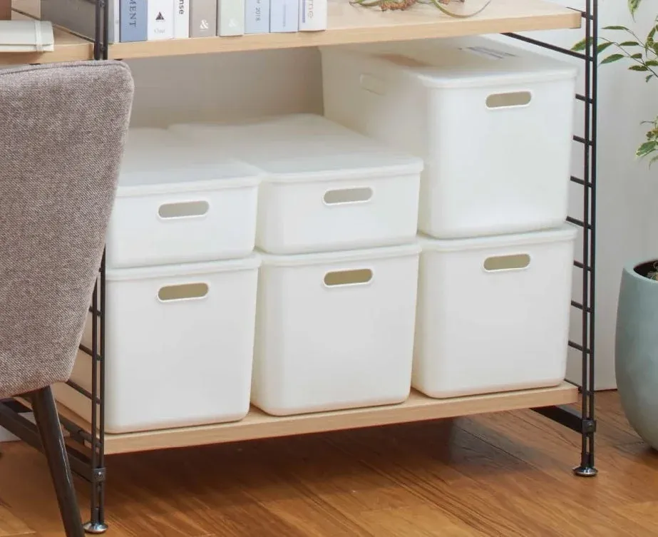 白い収納ボックスが木製の棚に整然と並べられ、すっきりとした整理された空間を演出しています。上段には本が置かれ、機能的でシンプルなインテリアの一角です。