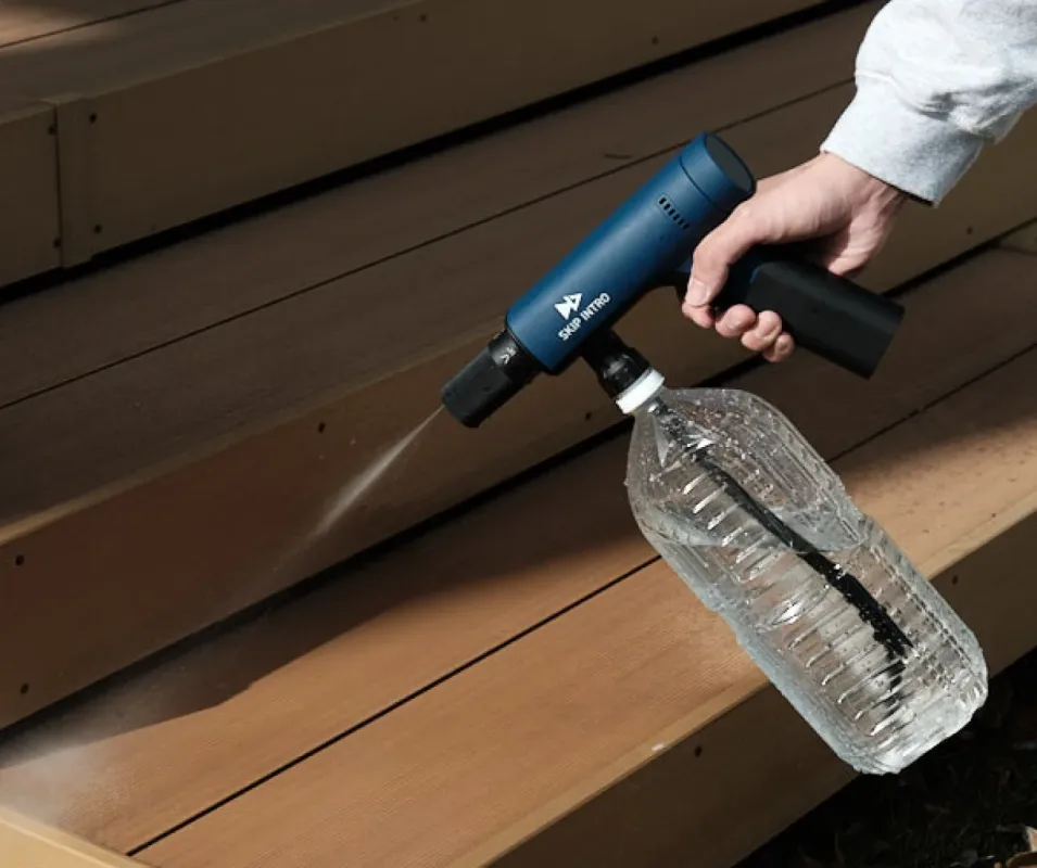 屋外の木製階段で、青いポータブルウォッシャーがペットボトルに取り付けられ、水が噴射されている様子