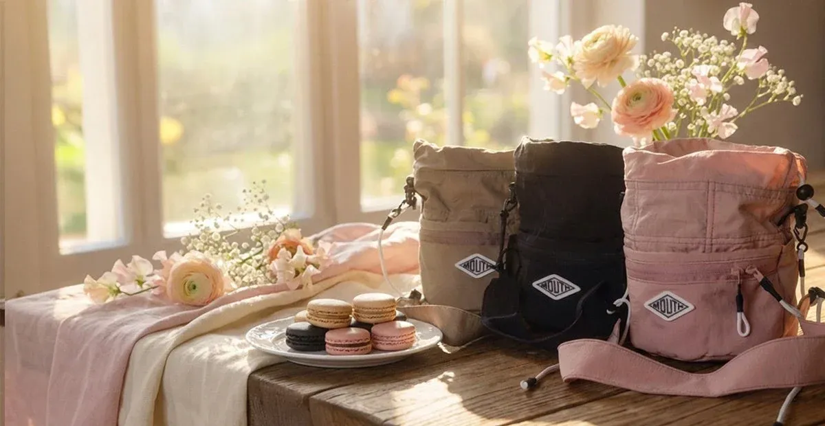 窓からの光が差し込むテーブルに並べられた3色のドローストリングバッグ、マカロン、花