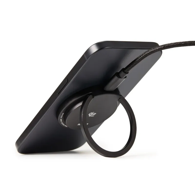 黒いスマートフォンが、背面に装着されたリングスタンドで立てられています。ワイヤレス充電対応のスタンドで、充電ケーブルも接続されています。