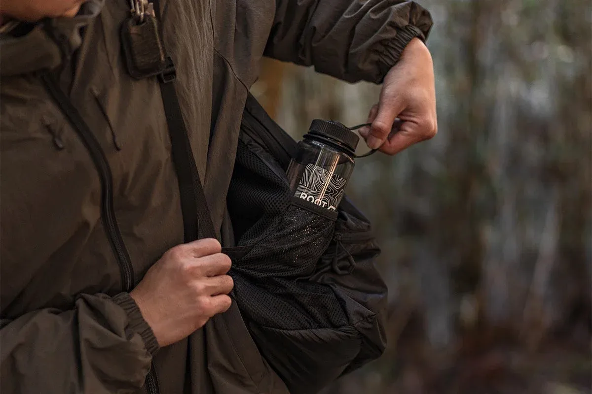 アウトドアウェアを着た人物が、バックパックのサイドポケットから「ROOT.C」と書かれたクリアな水筒を取り出している