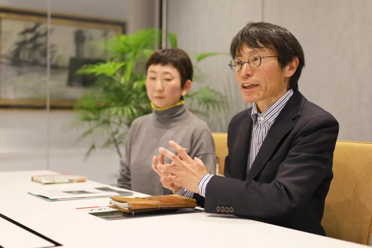 会議室で、スーツを着た男性が身振り手振りを交えて話し、隣の女性が耳を傾けているビジネスシーン