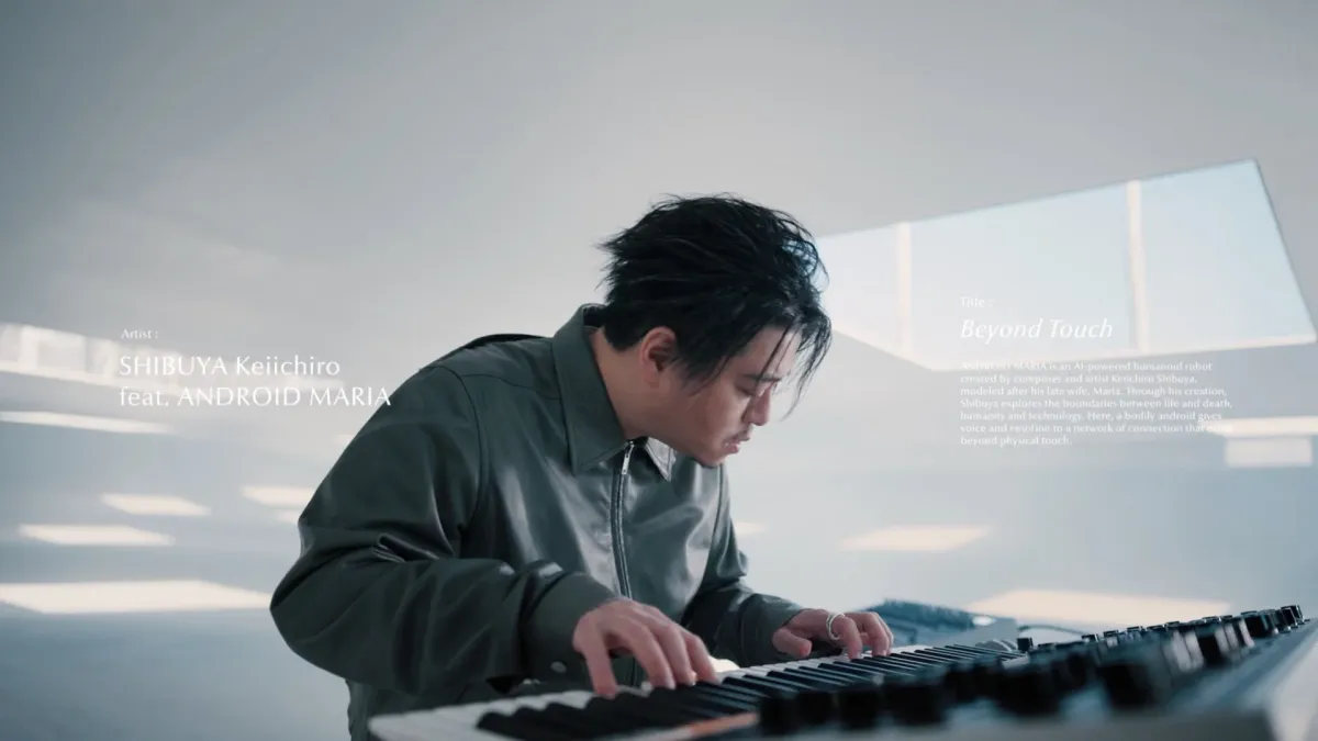 渋谷慶一郎がキーボードを演奏する姿と、彼が創造したAIロボット「アンドロイドマリア」との作品「Beyond Touch」の解説が写る