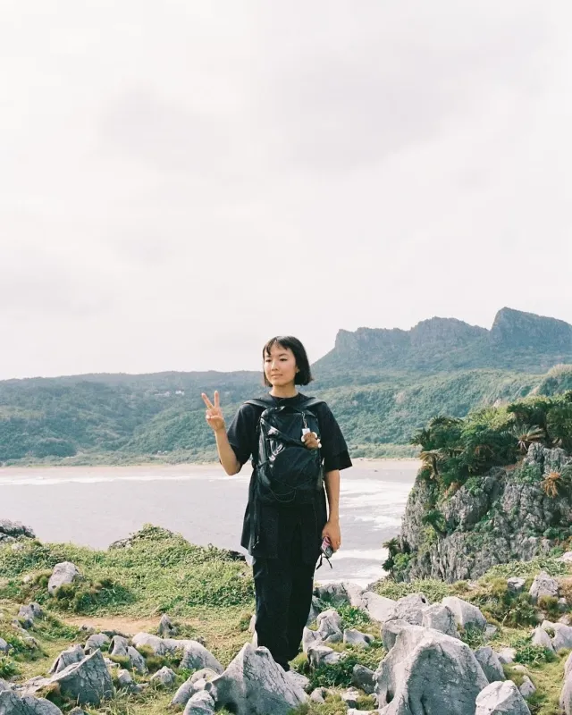 海と山を背景にピースサインをする女性