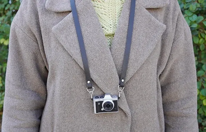 コートを着た人物が首からミニチュアカメラを下げている