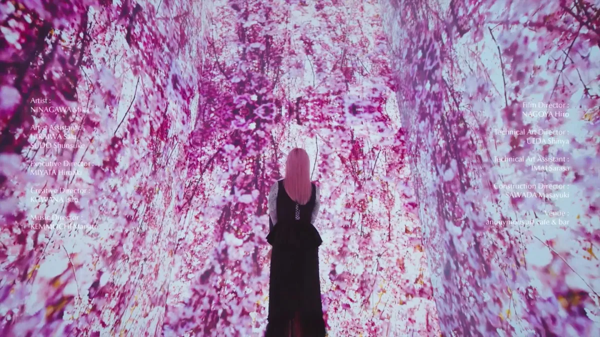 ピンクの髪の女性が、桜のプロジェクションマッピングに囲まれた幻想的な空間に立つアート作品のクレジット画面