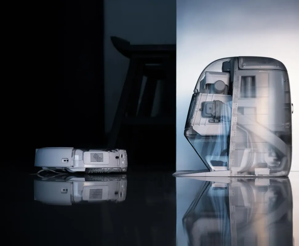 暗い床に置かれた白いロボット掃除機と、内部構造が見える透明なドッキングステーションが写っています。モダンで洗練されたデザインが特徴です。