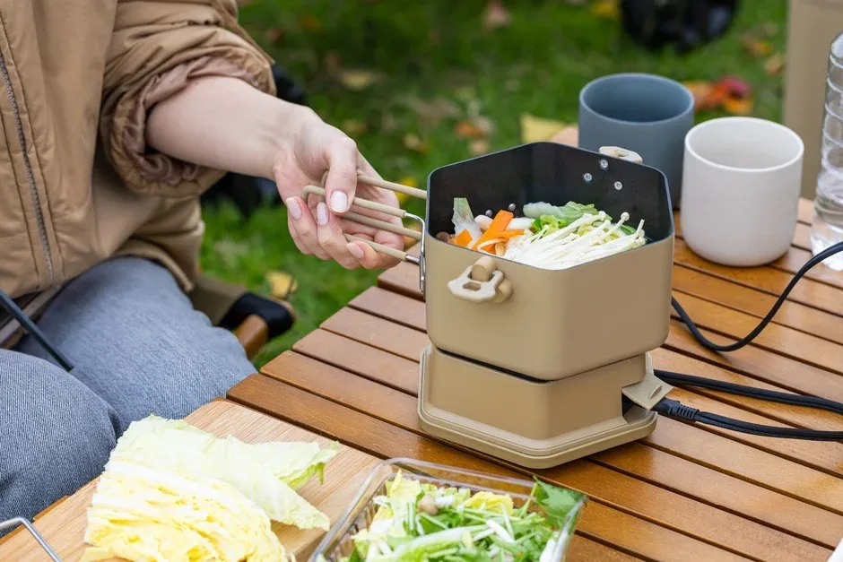 屋外で女性がポータブル電気鍋を使って野菜を調理している様子